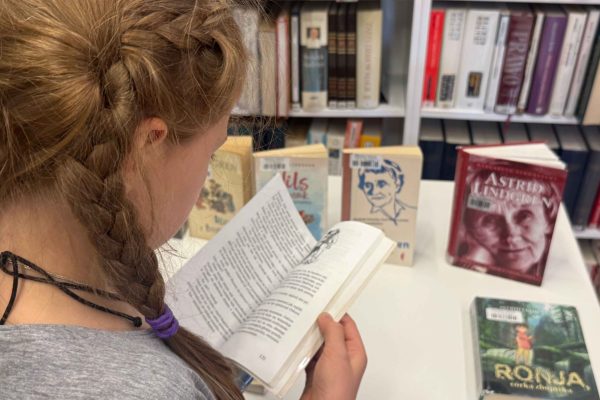 Zdjęcie dziewczynki czytającej książkę Astrid Lindgren. W tle inne książki szwedzkiej pisarki.
