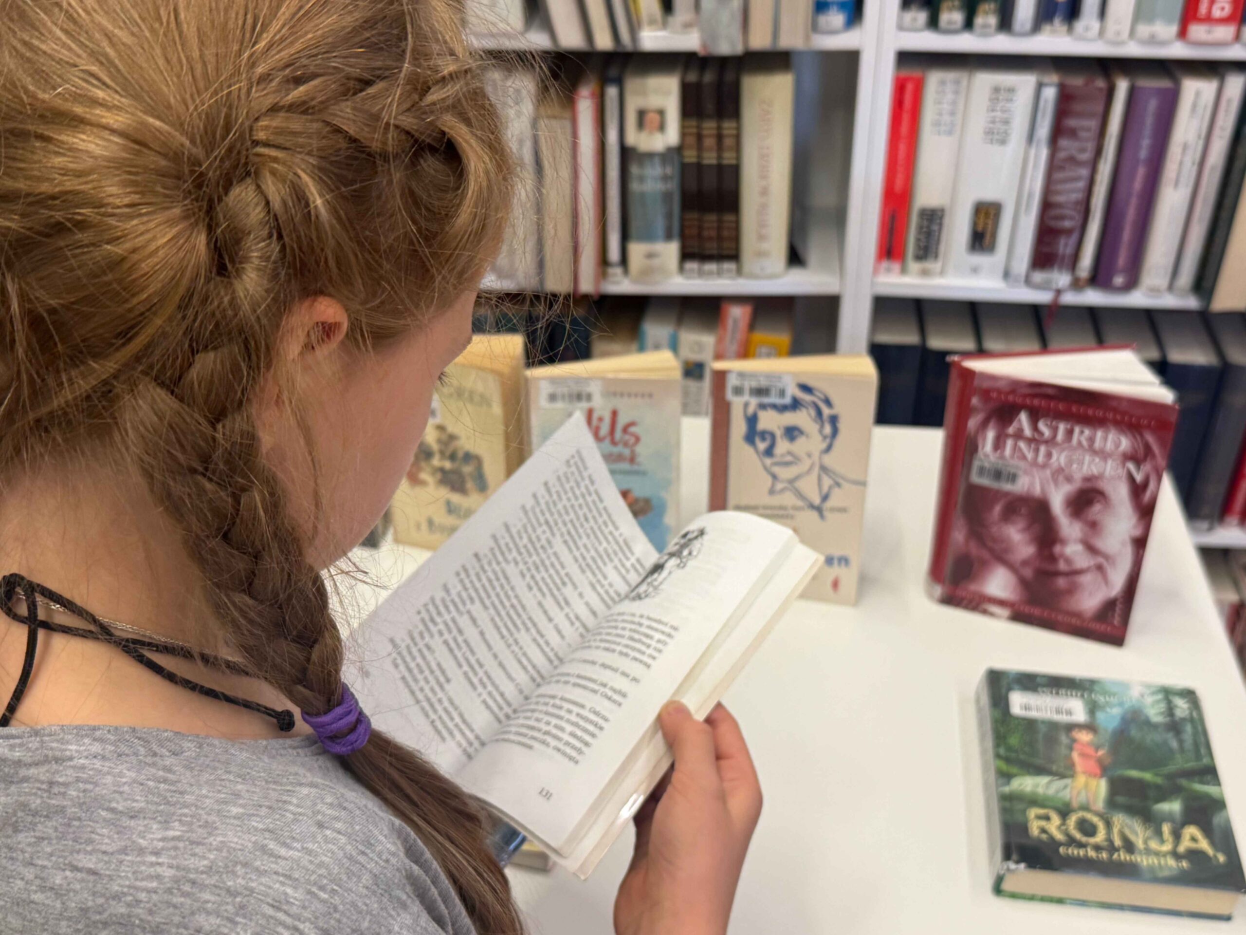 Zdjęcie dziewczynki czytającej książkę Astrid Lindgren. W tle inne książki szwedzkiej pisarki.