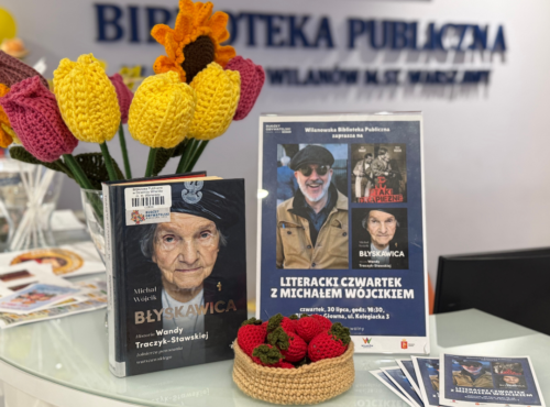 Wypożyczalnia Biblioteki na Kolegiackiej. Po lewej książka "Błyskawica", w tle kwiaty zrobione na szydełku, przed książką truskawki zrobione na szydełku. Po prawej plakat informujący o spotkaniu